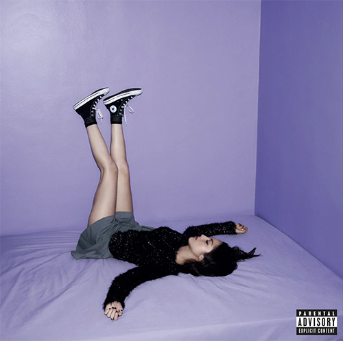 Album cover of Olivia Rodrigo's "GUTS". Cover shows Rodrigo, a woman with long black hair and wearing a black sweater and grey skirt, lying on a lavender bed with her legs resting up against lavender walls.