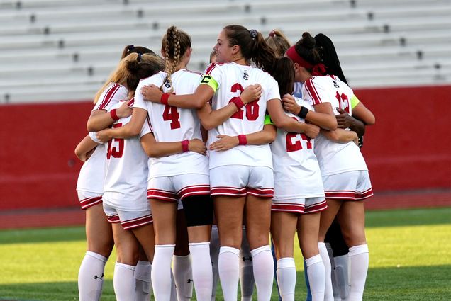 Photo: The BU Women's soccer team in red and white jerseys huddle at a recent match
