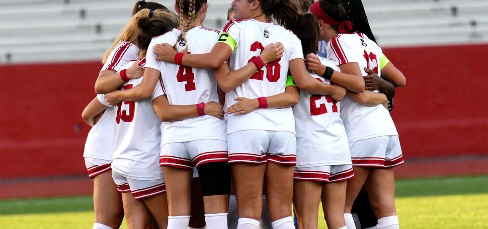 Photo: The BU Women's soccer team in red and white jerseys huddle at a recent match