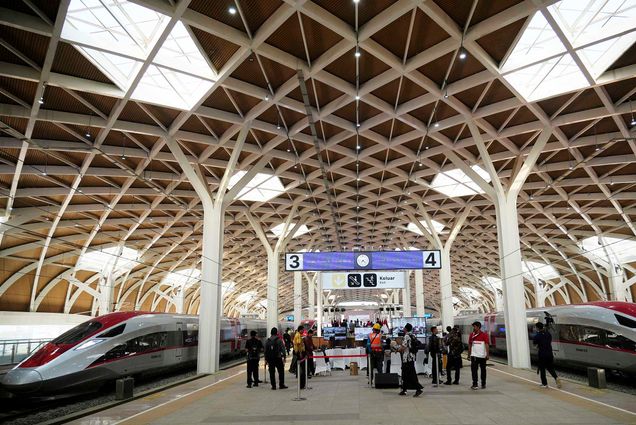 Photo: A red and silver high-speed train is parked during the opening ceremony for launching Southeast Asia's first high-speed railway at Halim station in Jakarta, Indonesia on Oct. 2, 2023. People stand under a large banner set up on the middle platform of the open-air train station.
