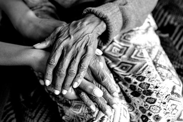 Photo: Black and white close up shot of an older, Black women's hands resting on a blanket.