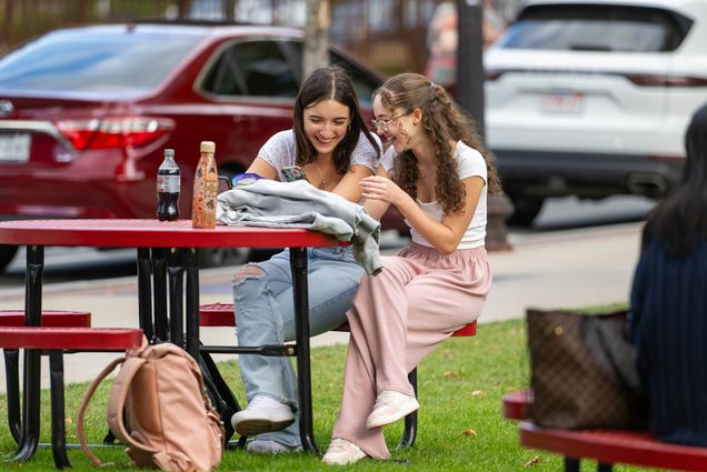 Photo: Two young women dressed in casual summer wear sit at a red table and laugh together.