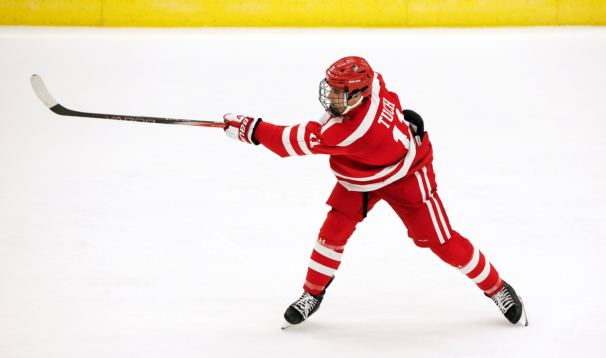 Photo: Luke Tuch, a young man wearing a red BU men's ice hockey helmet and uniform, takes a shot on the ice during a game.