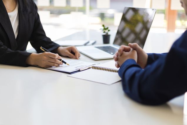 Photo: Two people sit at a desk for an interview in an office, one is looking at a resume