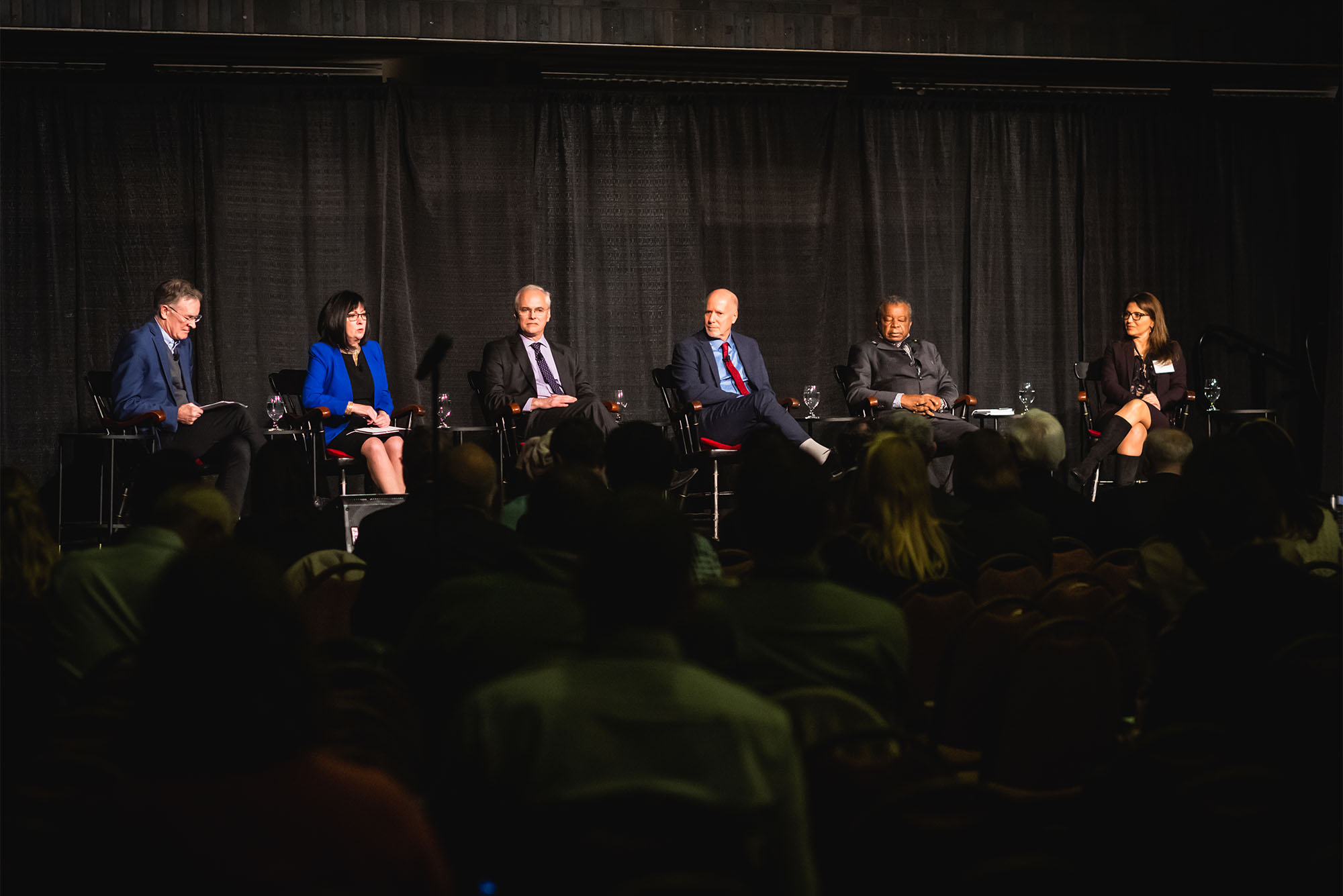 Photo: A panel of formally dressed individuals giving a presentation in front of a crowd