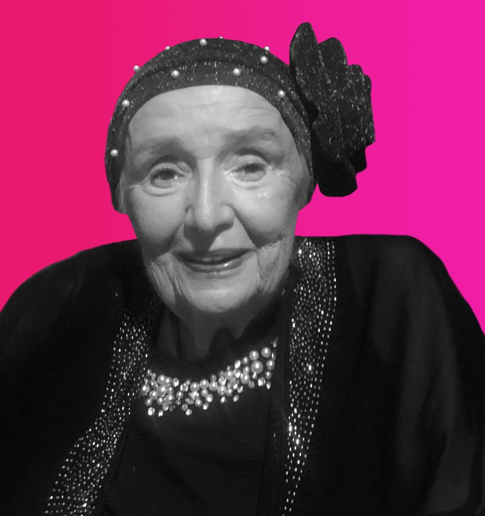 Photo: A cut out of Audry Lynch, a woman with a hair scarf, smiling for the camera. A fuchsia gradient is the background.