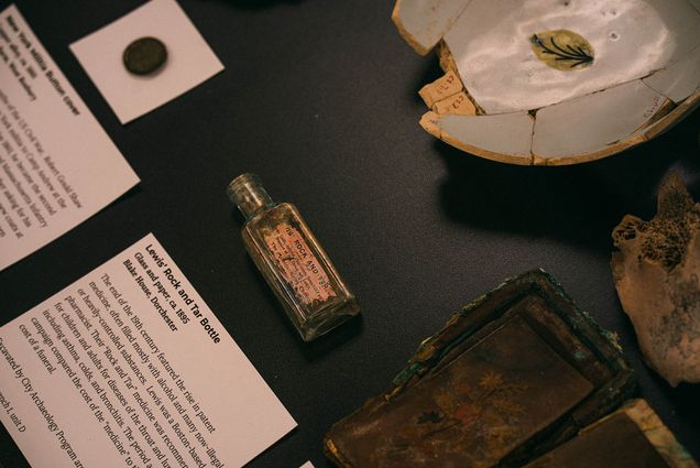 Photo: An overhead shot of a few items on display at the Mary C. Beaudry Community Archaeology Center. An old glass medicine bottle is featured in the center of a black table.