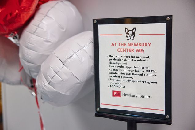 Photo: A sign that reads "At the Newbury Center We run workshops, have social opportunities, mentor students, and more!" is shown. To the left of the sign a group of red and white balloons is on display.