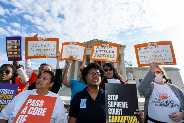 Photo: A diverse group of people holding signs protesting corruption in the Supreme Court and asking for a code of ethics are shown standing and protesting outside the Supreme Court building.