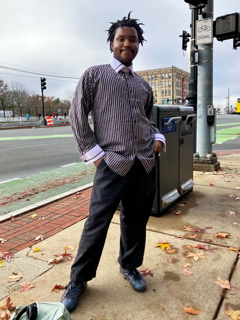 Photo: A black college student with a gray collared shirt and black pants standing on a busy street in Boston