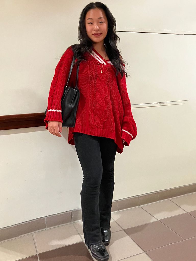 Photo: a college student with long dark hair wearing a red sweater and black pants with nice black shoes