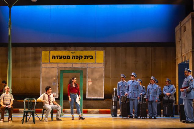 Photo: Two groups of people stand and perform on a stage. People dressed as Israeli villagers (left) host an Egyptian police band (officers dressed in blur uniforms) who stand to the right of the stage.