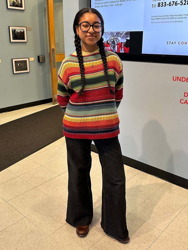 Photo: A college student with long dark braids wearing a colorful striped sweater and black jeans