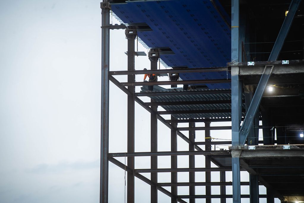 Photo of a construction worker at the edge of a platform of the data sciences building. the sky behind them is overcast, and the building is mostly exposed beams.