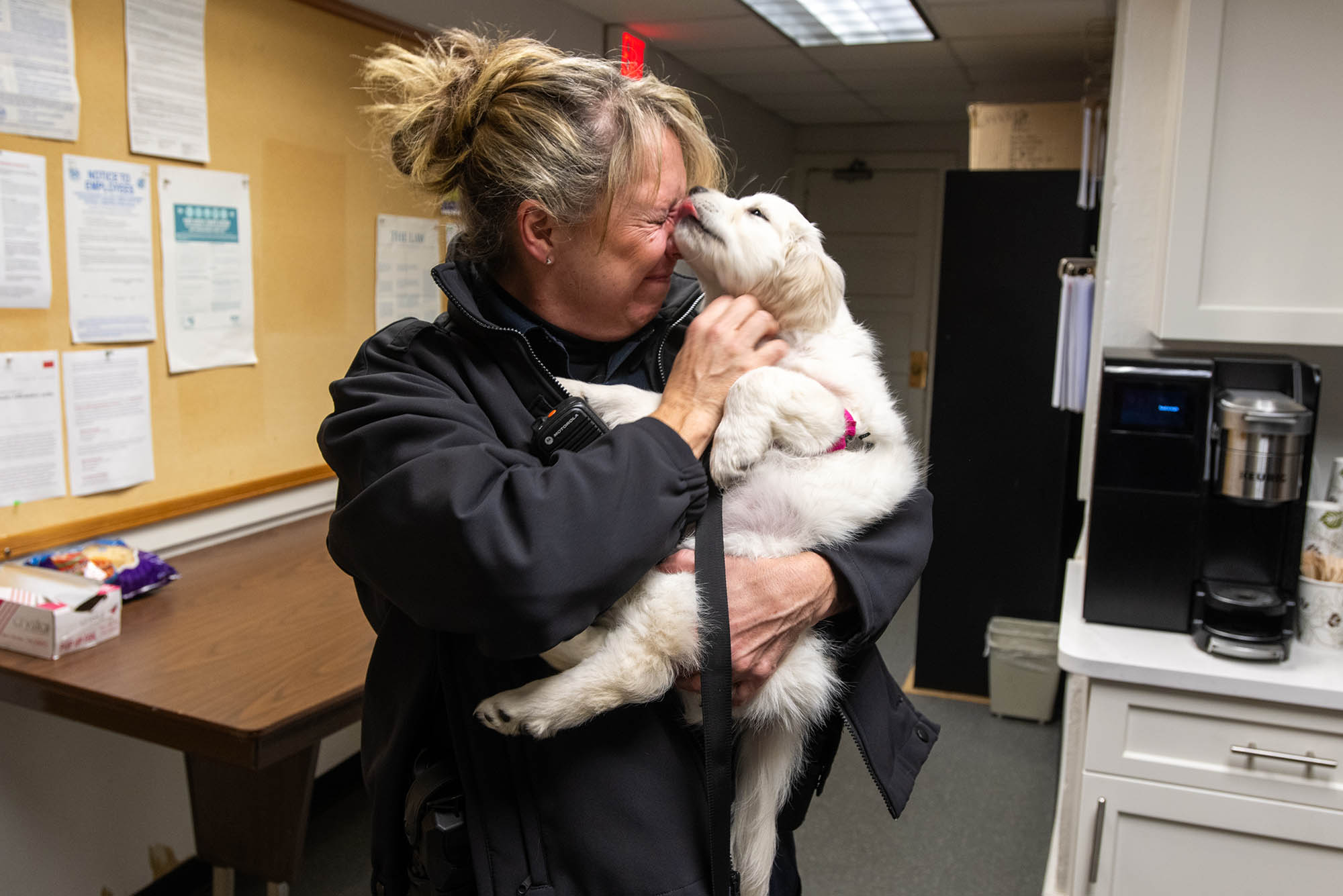 Photo: A white, fluffy 10-month old golden retriever licks Patrolwoman Diane Smith, a white woman with blonde hair, face while she holds her.