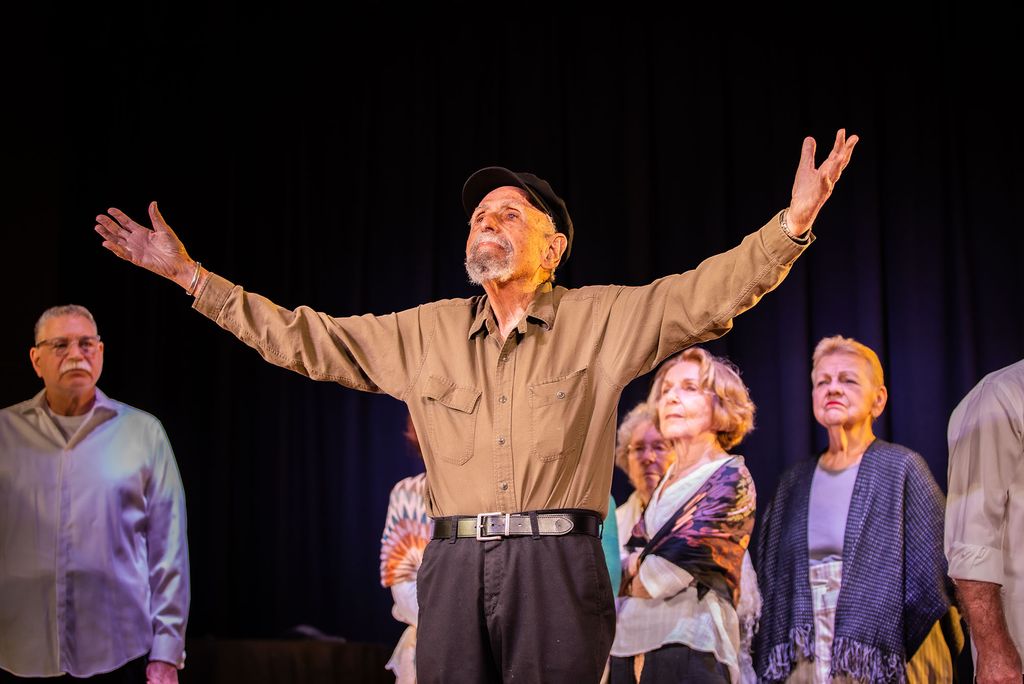 Photo: An older gentleman stands on a stage with his hands outstretch toward the sky, he appears to be singing