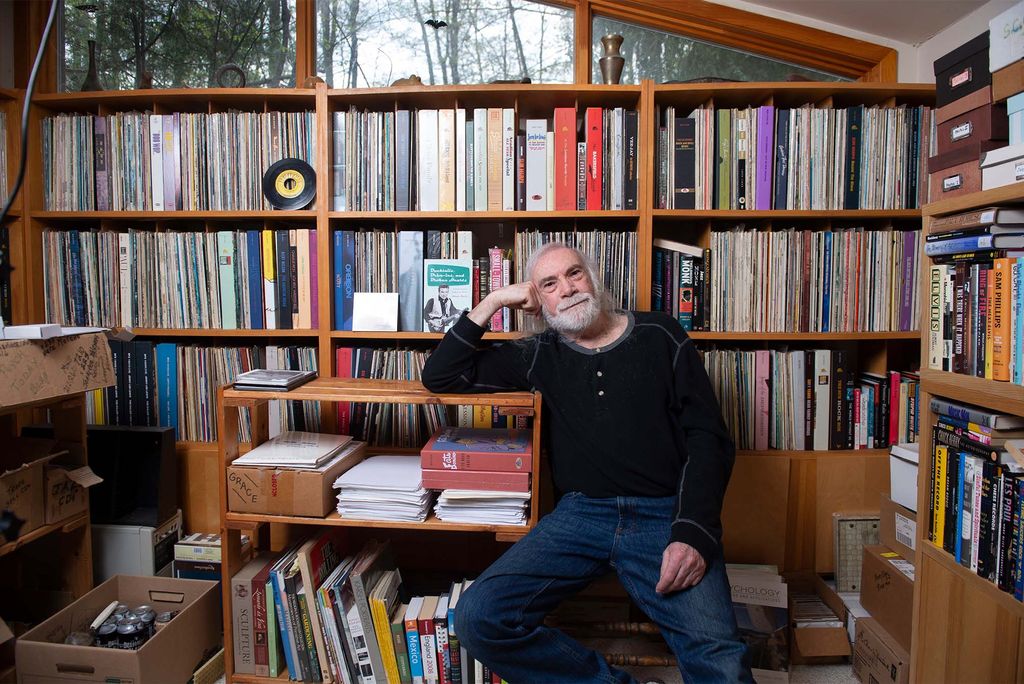 Photo: An older man sits in front of a wall full of old records and LPs