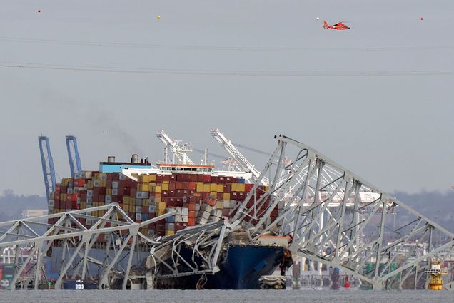 Photo: A helicopter flies over a container ship as it rests against wreckage of the Francis Scott Key Bridge after the container ship ran into the bridge, causing the collapse.