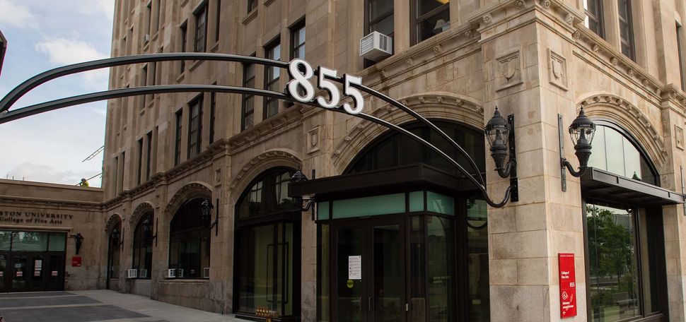Photo: A large building with tan-colored stone and black doors. There is a black metal arch with the numbers "855" outside of it