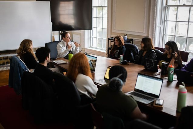 Photo: A classroom of people sitting around a large table with laptops open