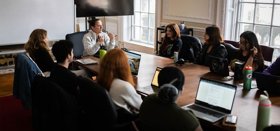 Photo: A classroom of people sitting around a large table with laptops open