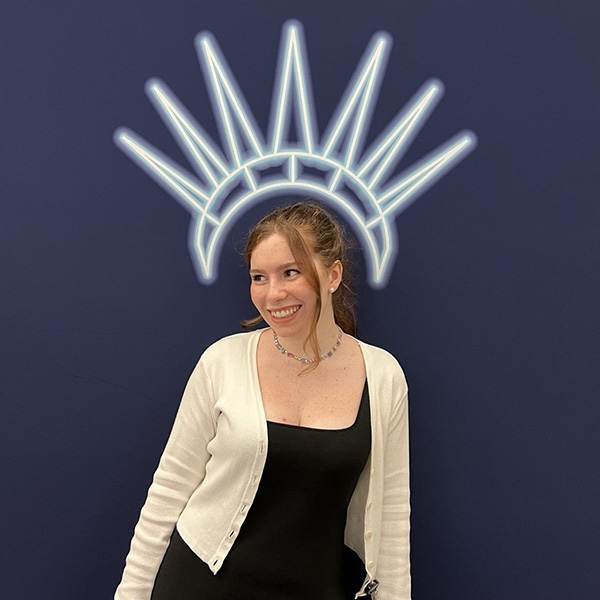 Photo: A young college student with red hair stands underneath a painting of a tiara on the wall behind them