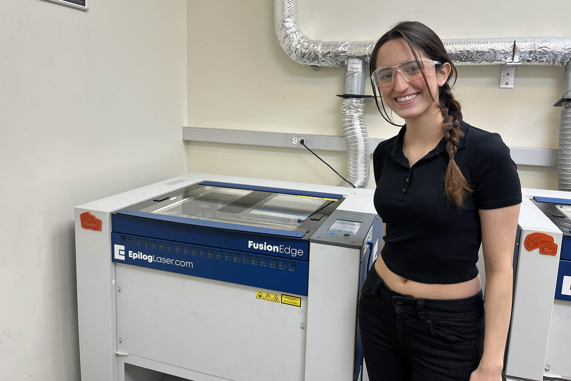 Photo: Cristina Colberg, a white woman with long brown hair and an all black outfit, waiting for her laser cutter creation.