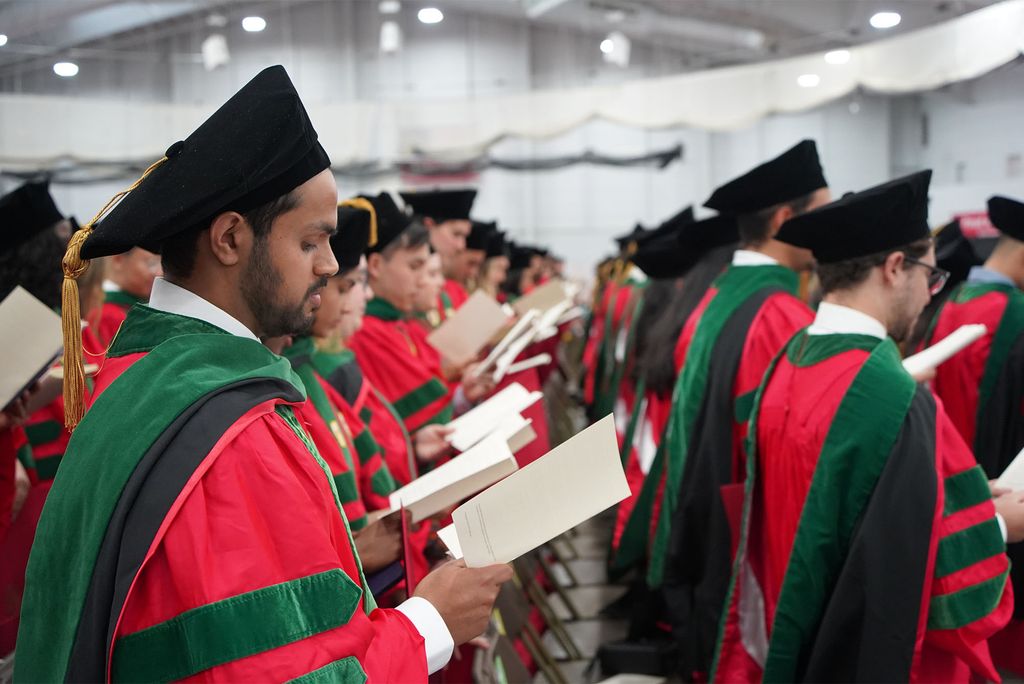 Photo: Newly minted doctors wearing red robes and doctoral hoods recite the Hippocratic Oath at the conclusion of the Chobanian & Avedisian School of Medicine’s MD and PhD convocation ceremony May 16 at the BU Track & Tennis Center