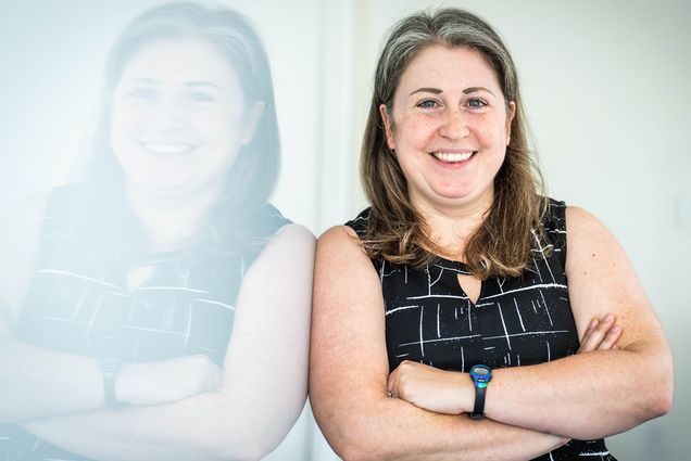 Photo: A white woman with midlength hair stands with arms crossed and a smile