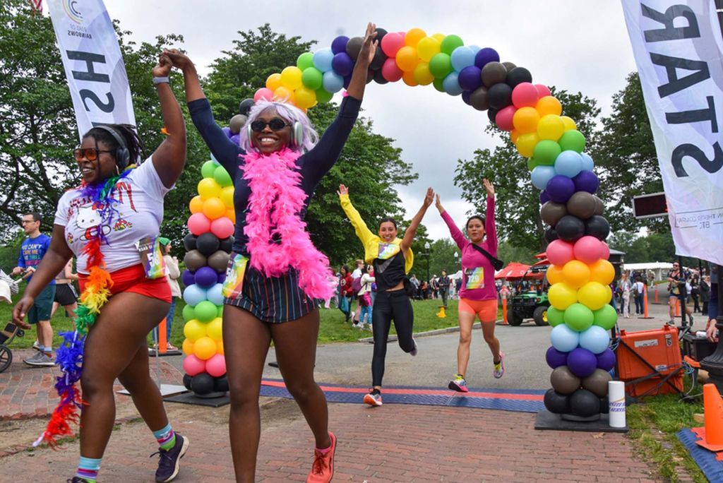 Photo: A picture of people completing a 5k by running under a vibrant, rainbow balloon arch