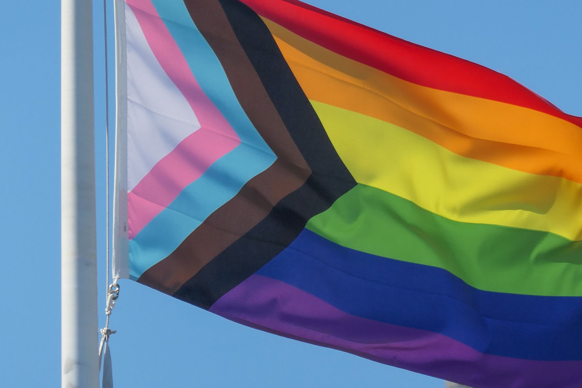 Photo: A picture of a pride flag being raised in front of a blue sky