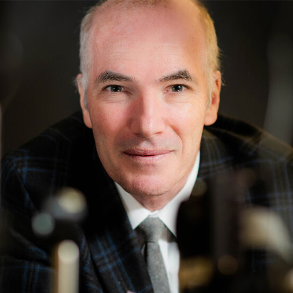 Photo: A headshot of a man looking into the camera. He is wearing a black suit with a blue plaid pattern on it