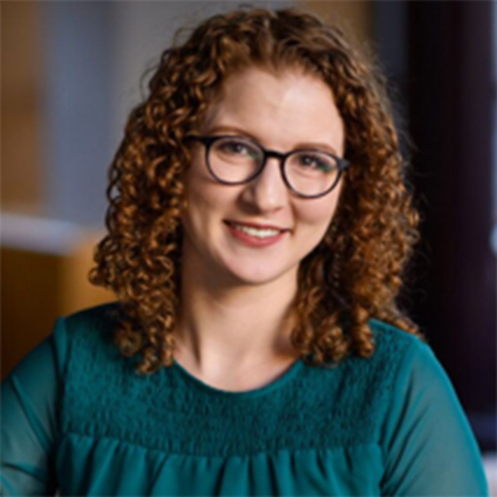 Photo: A picture of a BU professor posing for their headshot. She is wearing glasses and has mid-length brown curly hair