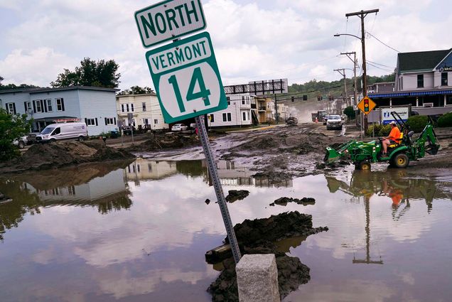 Photo: A small tractor clears water from a business as flood waters block a street.