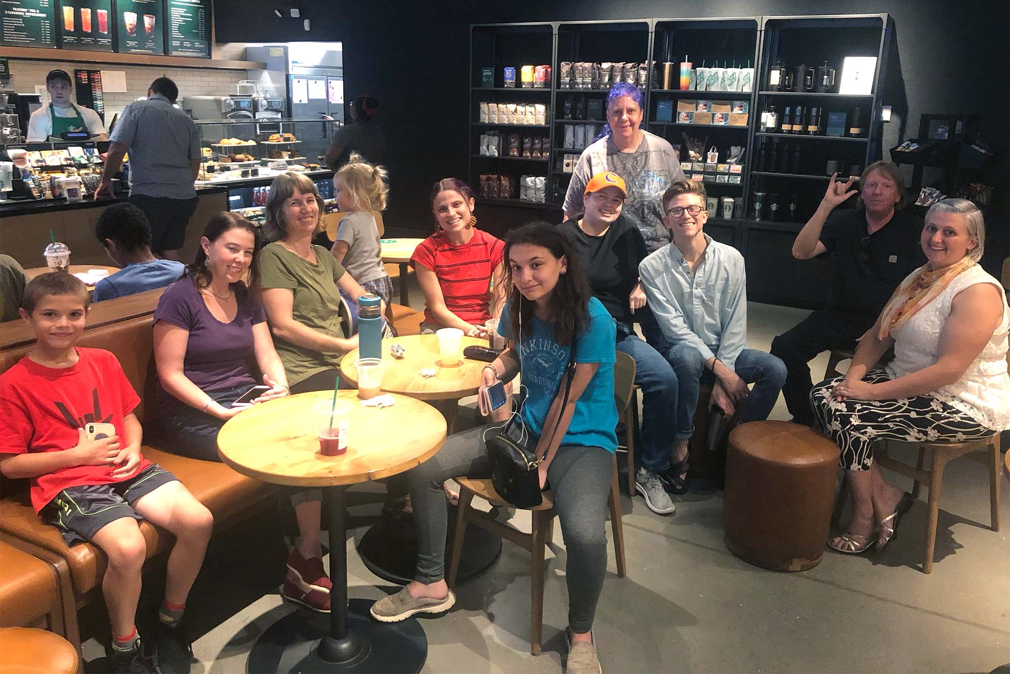 Photo: A group of individuals sit at tables at a local Starbucks. The wear various causal clothes as they look at the camera and smile.