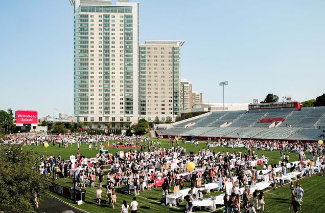 Photo: A large group of students standing on a soccer field in front of a large skyscraper