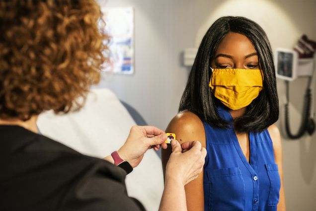 Photo: A black woman receives a band aid from a healthcare provider after receiving the COVID vaccine