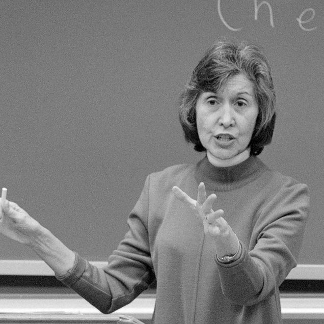 Photo: A black and white photo of a white woman teaching a class. She has short, dark hair and wears a tunic.