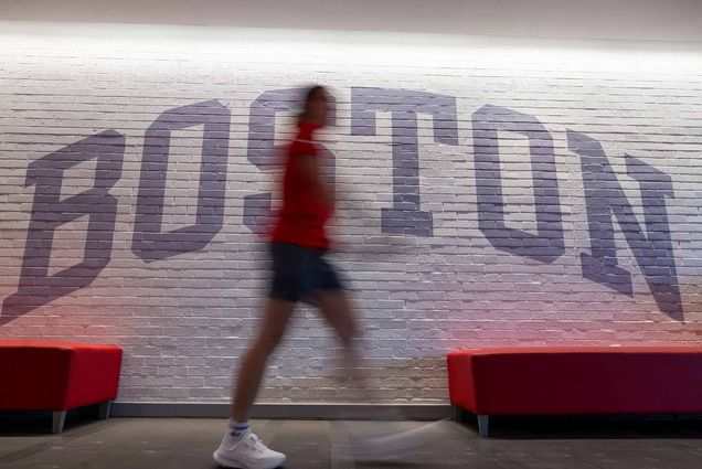Photo: Stock photo of a BU wall which reads BOSTON. A figure walks in front, blurred.