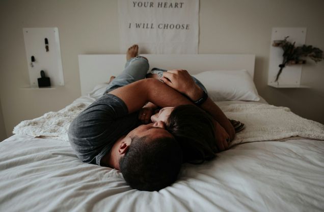 Photo: Two people, one with a tan skin tone, another with more fair skin tone, lay caressing on a bed with all white sheets. A motivational quote with the text ‘YOUR HEART I WILL CHOOSE’ written in bold, uppercase letters against a plain background.”