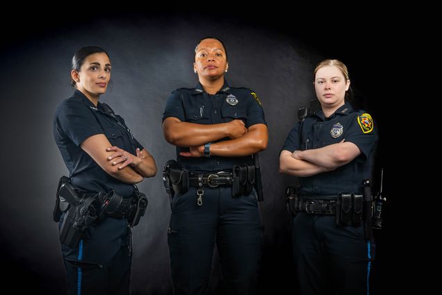 Photo: Three female police officers stand with arms crossed in full uniforms in front of a dark background