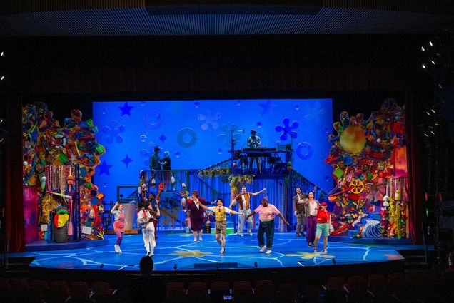 Photo: A wide shot of the stage during the Wheelock Family Theatre's production of "The Spongebob Musical." The set features lots of blues, to simulate being underwater, and the actors are in colorful attire. Along the side of the stage is colorful stacks of memorabilia