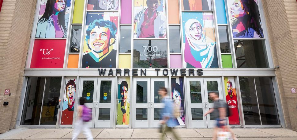 Photo: The outside of "Warren Towers," a building at BU. The outside of the building has a colorful mural of many people and there are students walking in front of the building on the sidewalk