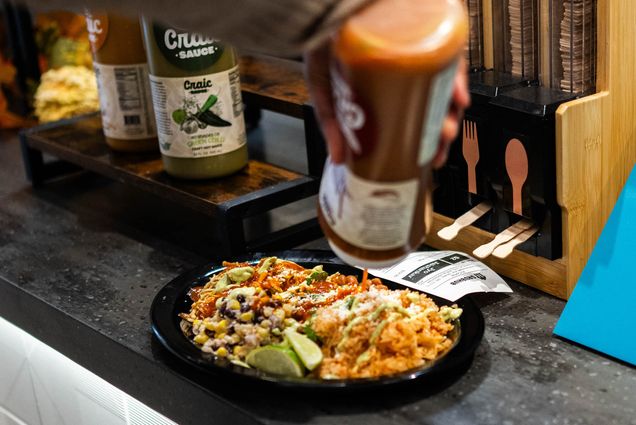 Photo: Someone holding a sauce bottle pours the contents on their plate of food.