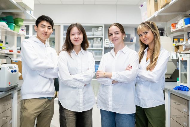 Photo: A picture fo four students in white, long-sleeve shirts with their arms crossed in a biology lab.