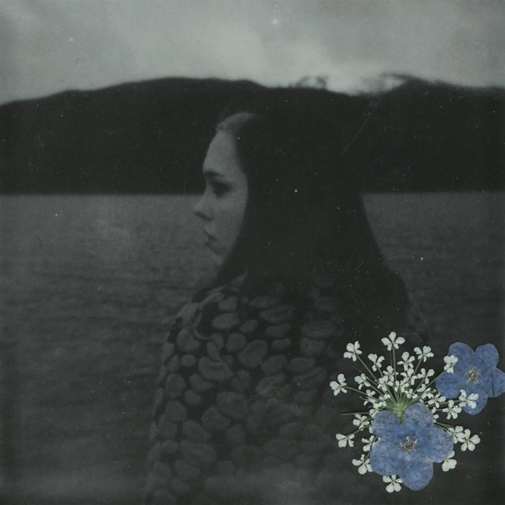 Photo: A black and white photo of a women frolicking in a field with a pressed flower in the bottom right hand corner.