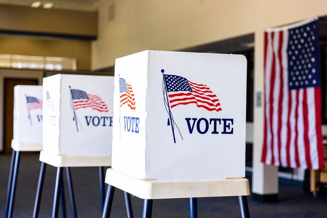 Photo: A picture of white voting booths on election day with an American flag illustration and "VOTE" written on each.