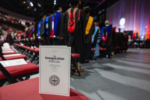 Photo: Program for Melissa L Gilliam's inauguration at BU's 11th President in September 2024, sitting on a chair at the event as the crowd applauds