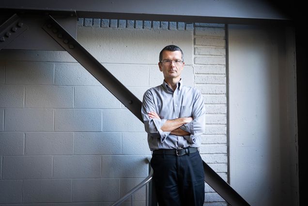 Photo: A man in a long-sleeve button down crossing his arms and leaning back. He has a very short haircut and glasses