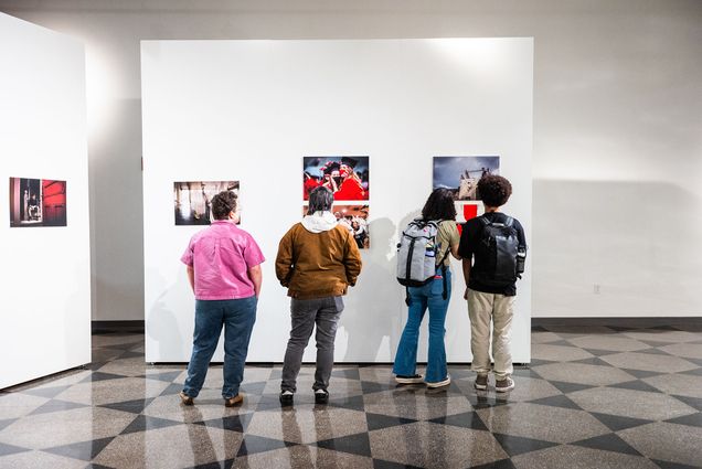 Photo: Four people standing and admiring photos on a gallery wall